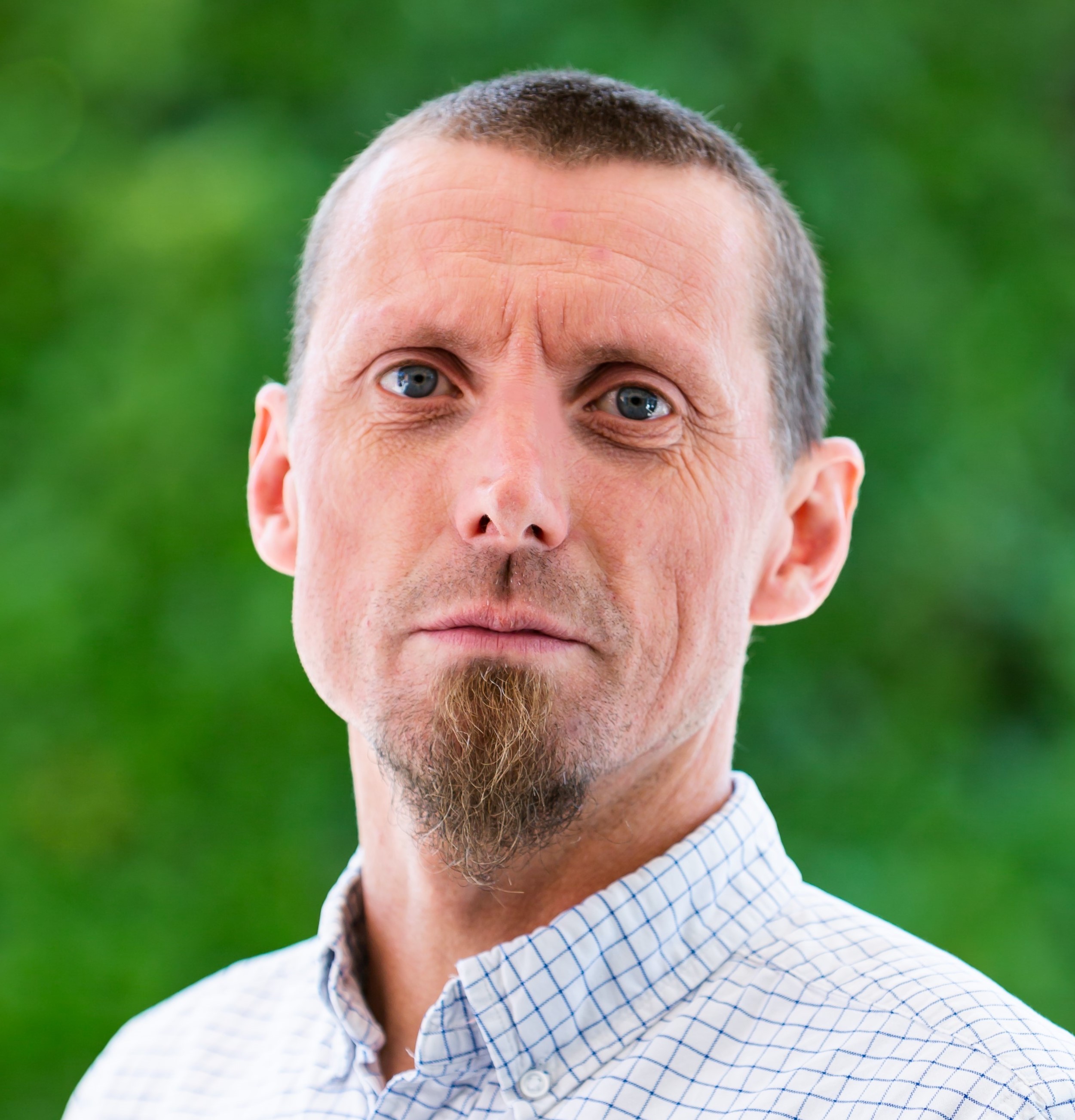Photo of Fil McIntyre, wearing a checked shirt, against a green outdoor background.